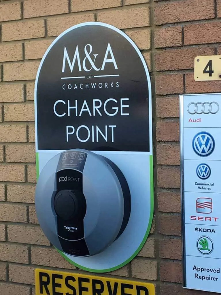 Printed charge point sign on a brick wall beside a column of vehicle brand logos