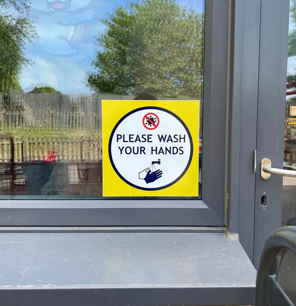 Yellow Please Wash Your Hands sign fixed beside a glazed school door