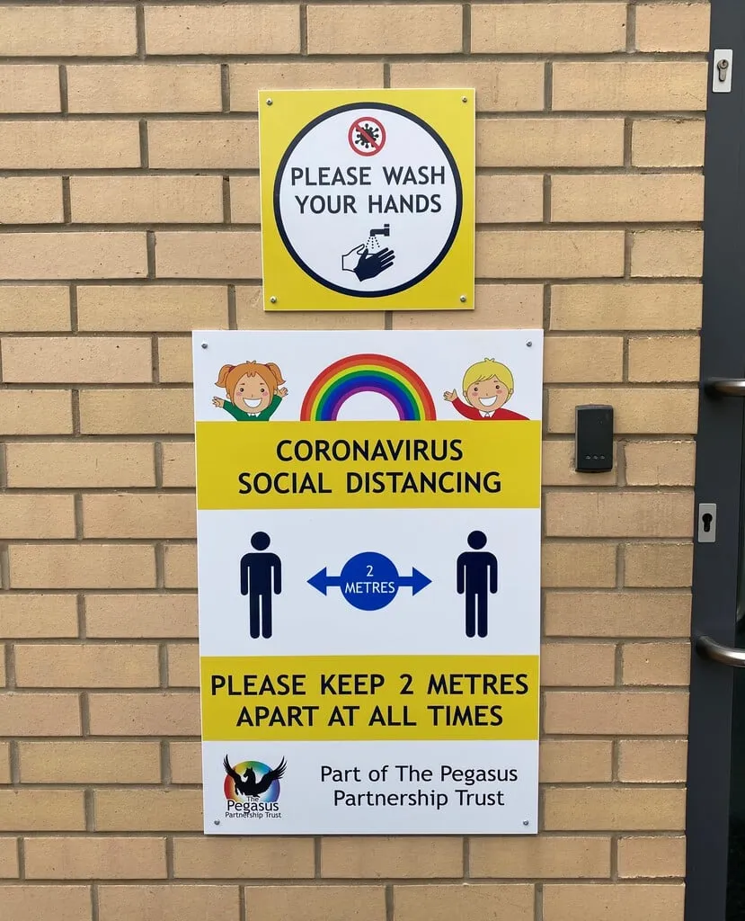 Please Wash Your Hands and Coronavirus Social Distancing signs mounted on a school brick wall