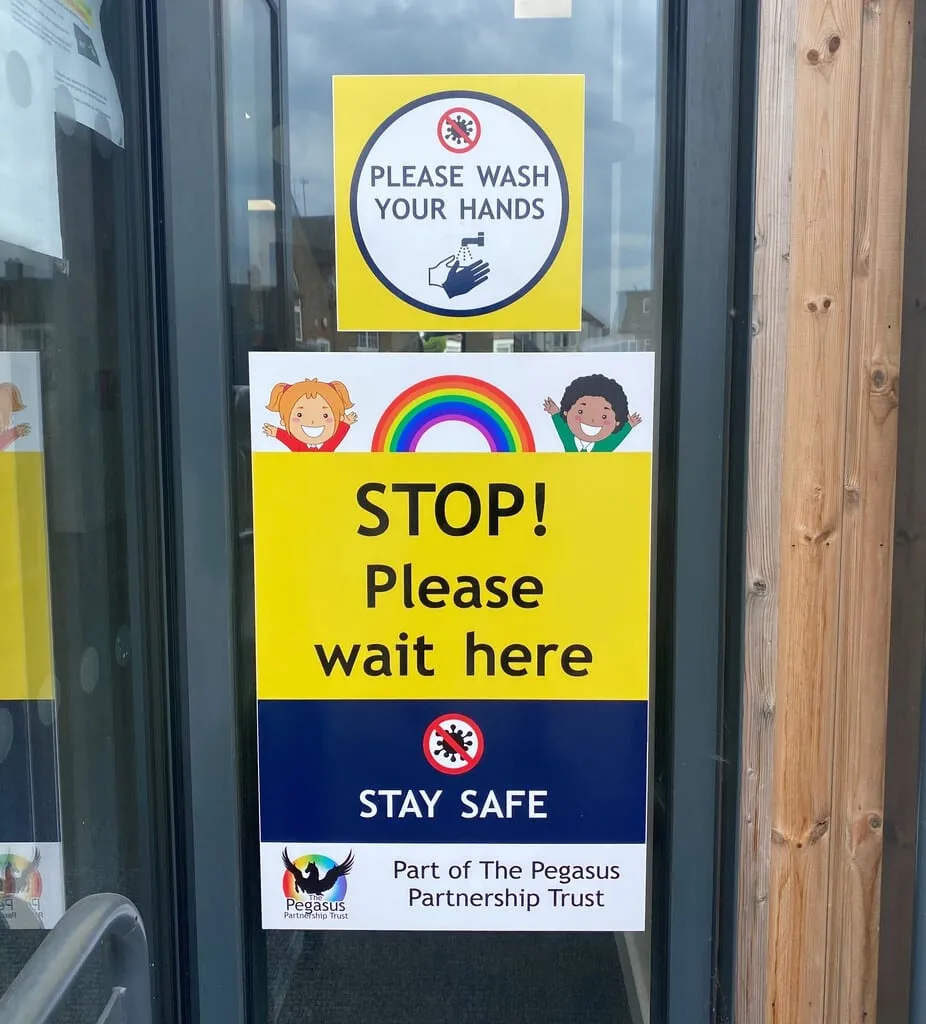Please Wash Your Hands and STOP Please Wait Here signs on a glazed school entrance door