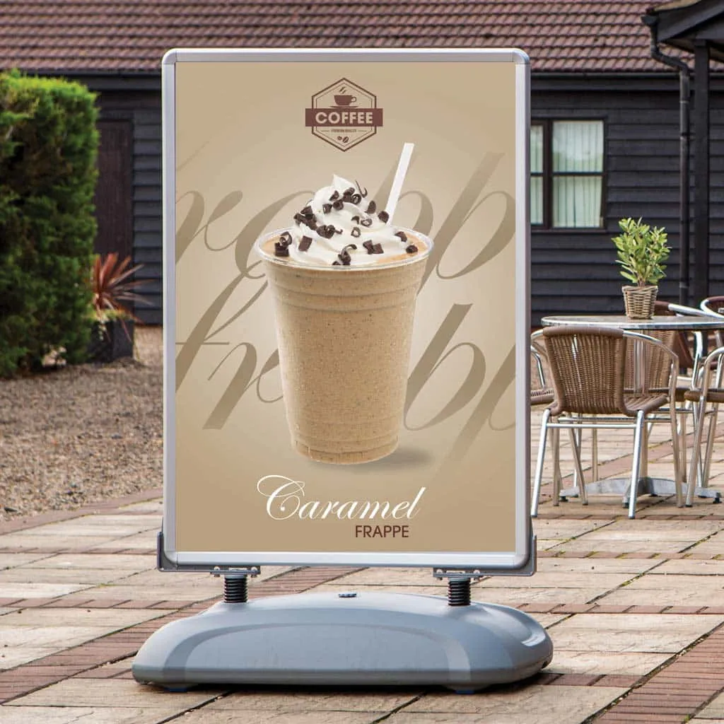 Spring mounted pavement sign advertising a caramel frappé outside a café