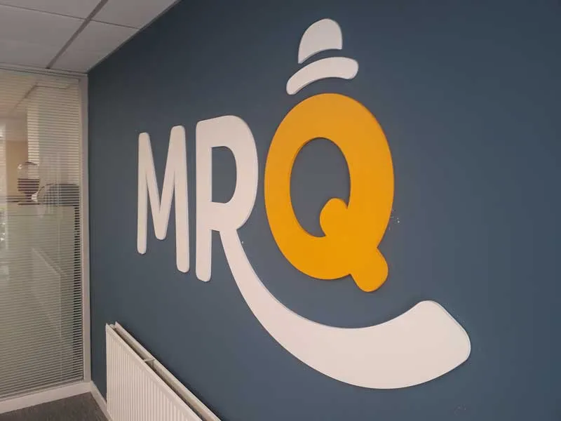 MRQ logo in white and orange three-dimensional letters on a dark blue office wall