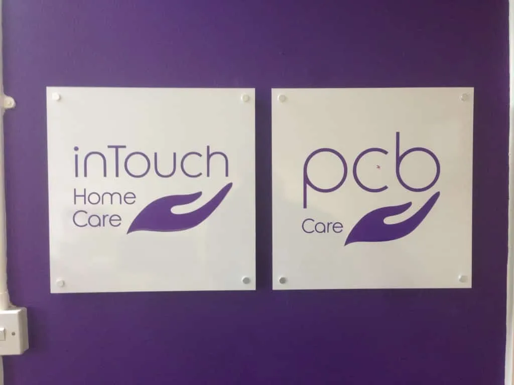 Two white wall plaques for inTouch Home Care and pcb Care mounted on a purple wall