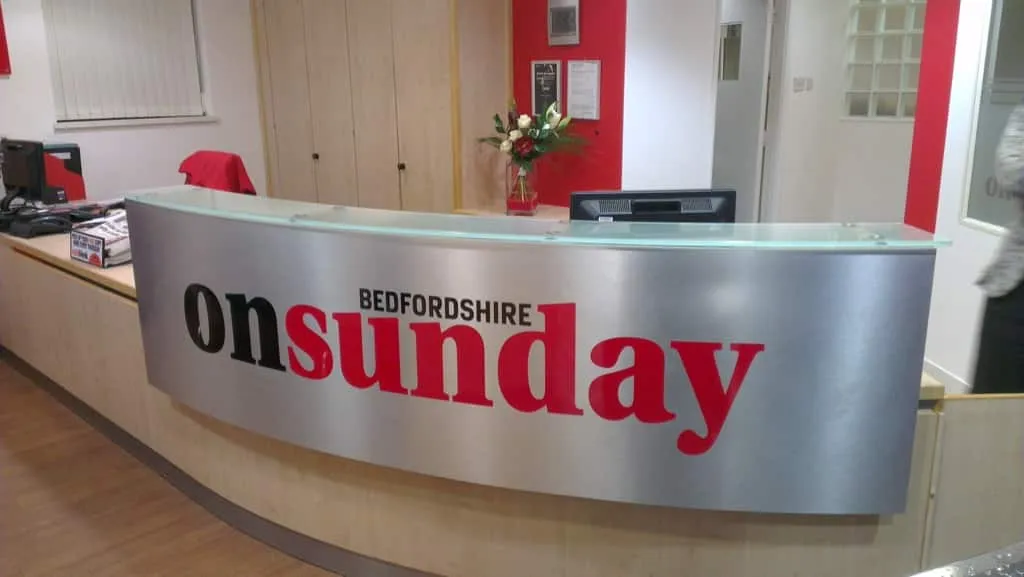 A curved brushed metal reception desk wrapped in on Sunday Bedfordshire graphics