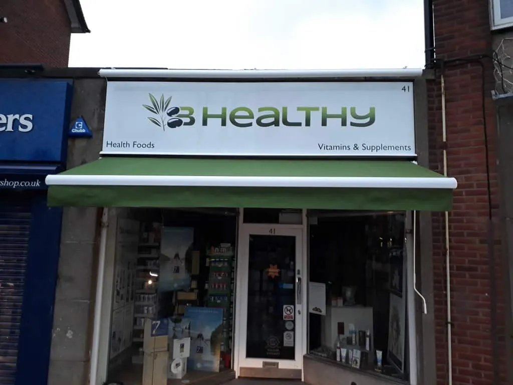 An illuminated fascia sign above a green awning for the B Healthy health food shop