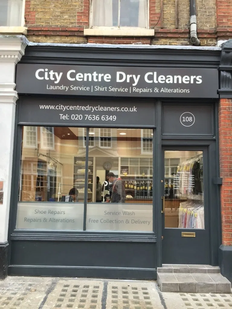 White fascia lettering and window graphics on the dark grey shopfront of City Centre Dry Cleaners