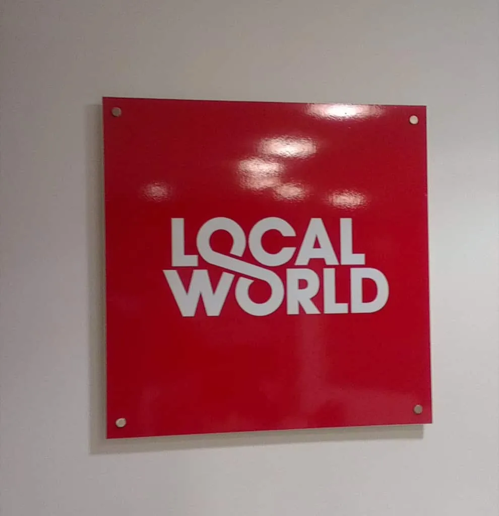 A red acrylic wall panel carrying the Local World logo in white, fixed on stand-off bolts