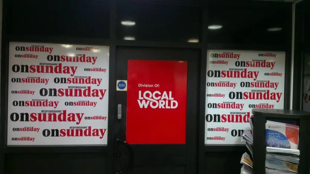 Repeated on Sunday window graphics and a red Local World poster on a dark shopfront at night