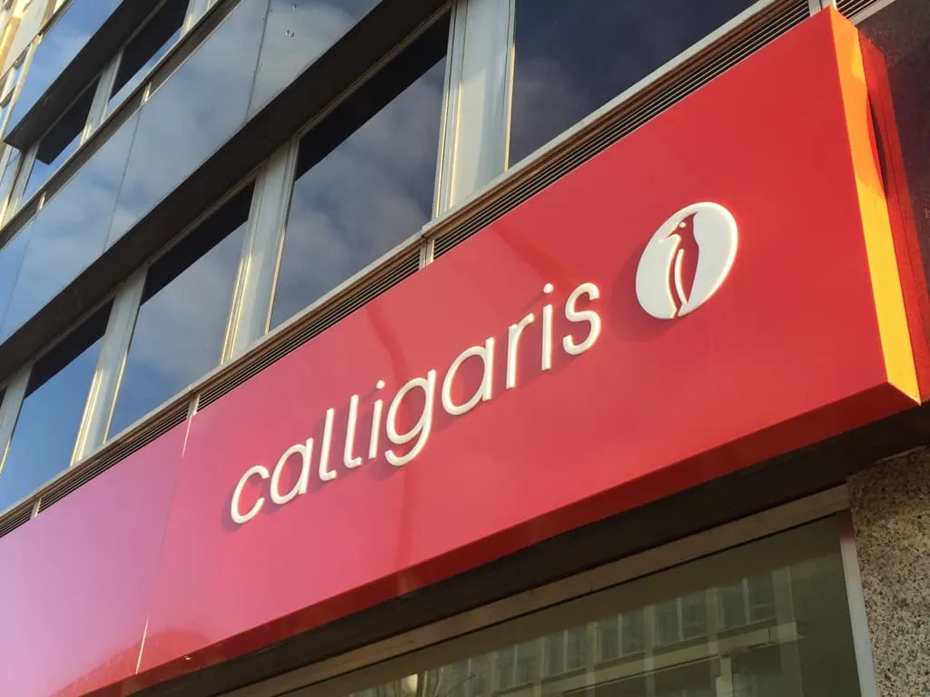A red illuminated fascia sign with white calligaris lettering above a showroom