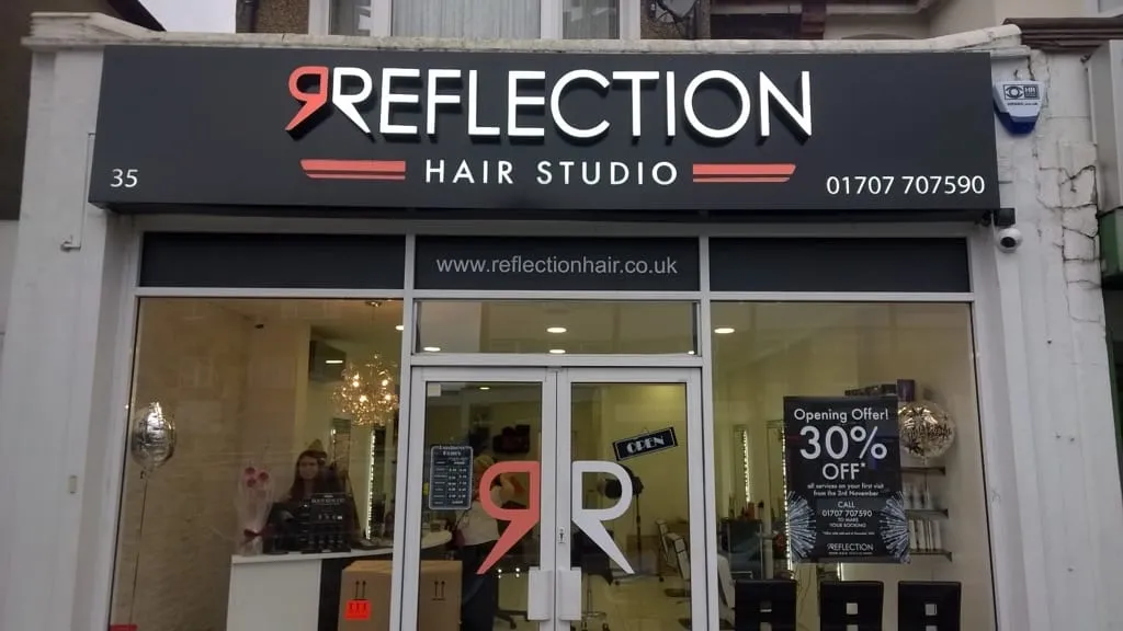 A black shopfront sign for Reflection Hair Studio with a red letter R motif